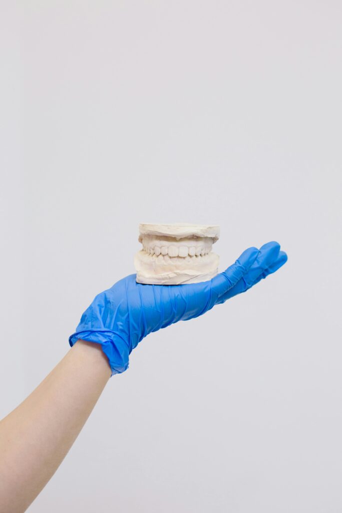 A gloved hand holds a dental mold showcasing teeth structure against a white background.